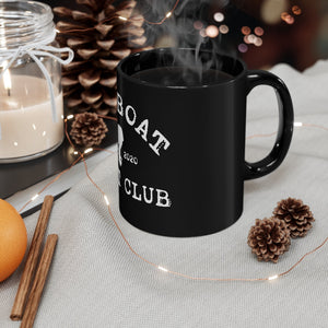 Steaming 11oz black ceramic mug with a white "BOAT CLUB" design, surrounded by pinecones and string lights.