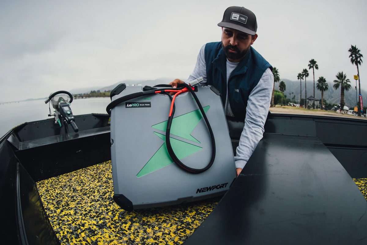 Man places a gray Newport LoPRO 48V 70Ah lithium battery with green logo and red handle into a boat.