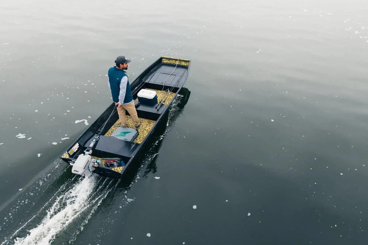 Man in a small, black flat-bottom boat with a white outboard motor, moving across calm water.