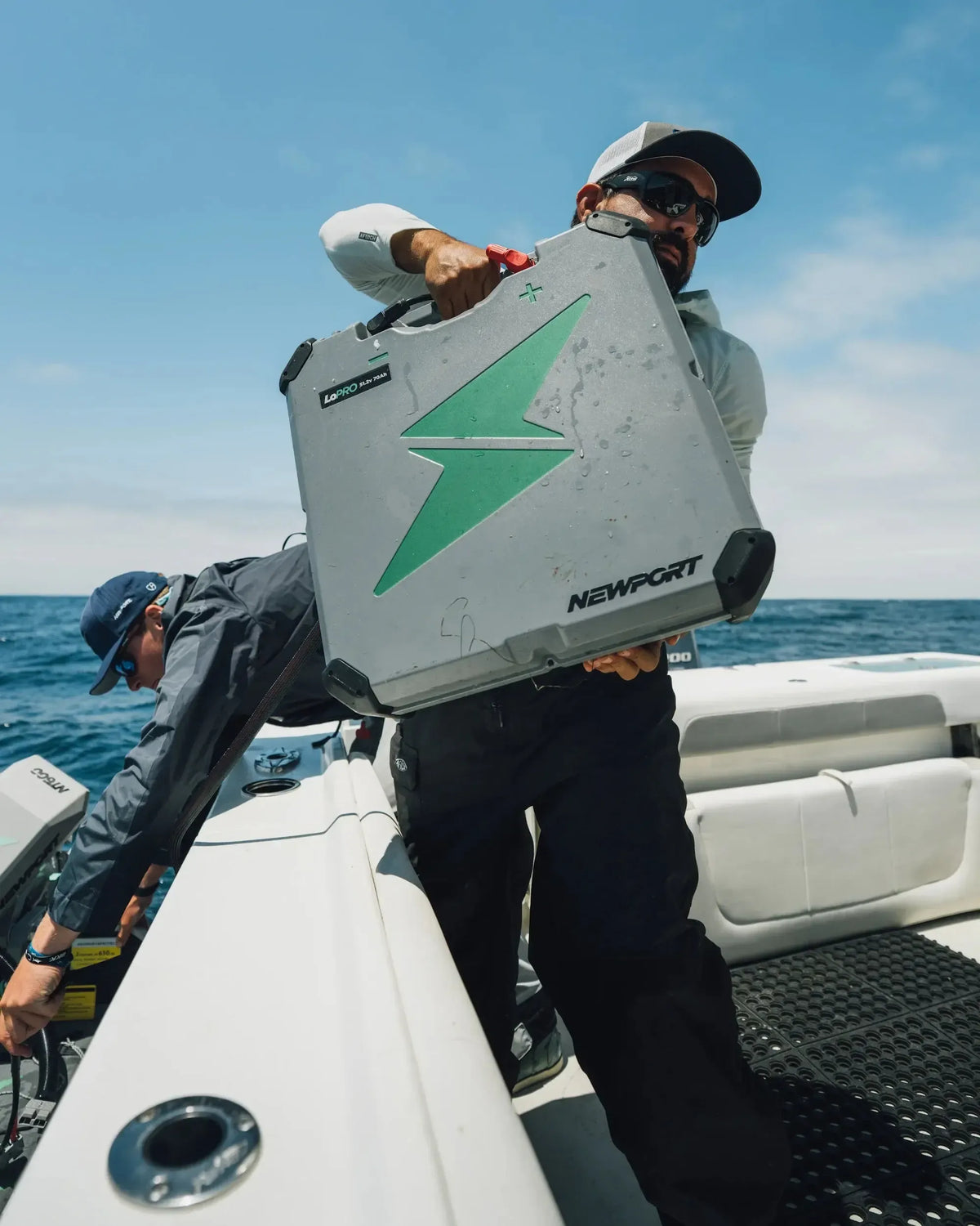 Man carrying a gray Newport LoPRO 48V 70Ah Lithium battery with a green lightning bolt logo on a boat.