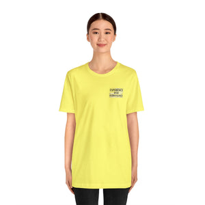 Woman wearing a yellow "American Dreamer" unisex short sleeve tee with "EXPERIENCE OVER EXTRAVAGANCE" text.