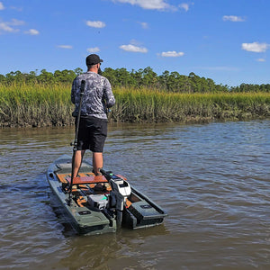 Angler standing in an olive Crescent Cres-Craft fishing skiff with a motor, on a calm river.