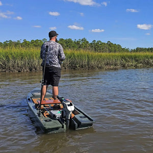 Angler standing in an olive Crescent Cres-Craft fishing skiff with a motor, on a calm river.