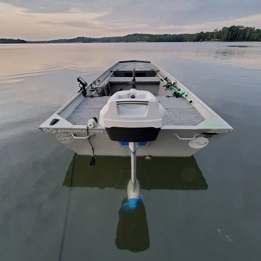 A motorized boat with an EPropulsion Spirit 1.0 Plus electric outboard motor, resting on the water with a trailer attached.