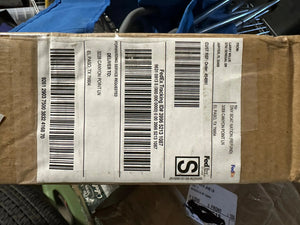A close-up of a brown cardboard shipping box with a large white FedEx tracking label, photographed in a cluttered storage or shipping area.