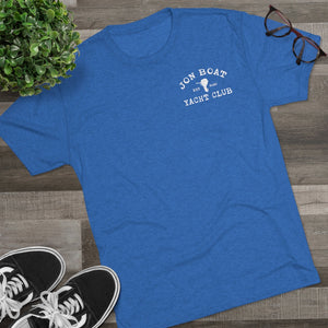Blue tri-blend Jon Boat Yacht Club regular fit tee with white graphic, shown on wood with plant and glasses.