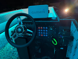 Boat dashboard with black steering wheel, Garmin display, and Plashlights REVERT 22mm switches with blue and red LED rings.