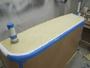 Light yellow pour foam expanding in a boat hull, with blue painter's tape along the edges.
