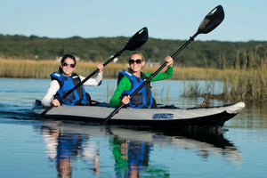 Two women paddling a gray and white Sea Eagle FastTrack inflatable kayak with black paddles.