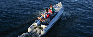 Two people in red life vests motor a white Sea Eagle 437ps PaddleSki inflatable catamaran on blue water.