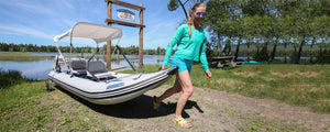 Woman carrying a white and gray Sea Eagle 437ps PaddleSki inflatable catamaran with a canopy.