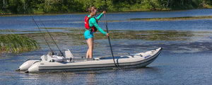 Woman standing on a gray Sea Eagle 437ps Paddleski inflatable catamaran boat, paddling on a lake.
