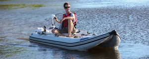 Man in red life vest operating a gray Sea Eagle 437ps PaddleSki inflatable catamaran with a trolling motor.