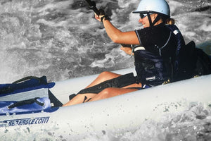 Smiling kayaker in a white helmet and black shirt, using black Sea Eagle thigh straps in a white inflatable kayak on choppy water.