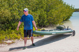 Man rolling a green Sea Eagle inflatable kayak on a sandy beach using the black EZ Cart.