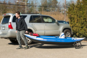Man smiling, pulling a blue and black Sea Eagle inflatable kayak on an EZ Cart with black wheels.