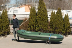 Man pulling a green inflatable boat with a black Sea Eagle EZ Cart (wide) with 14" wheels.
