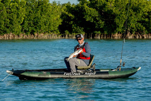 Man in a green inflatable kayak with a swivel seat fishing rig, holding a fish.