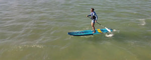 Man paddleboarding on a blue and yellow Sea Eagle LongBoard 11 inflatable SUP on calm water.