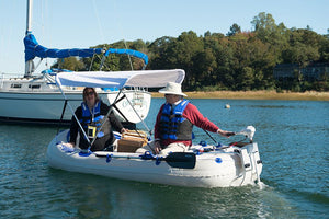 Two people in a white and blue inflatable Sea Eagle SE9 boat with a motormount and white sun canopy.