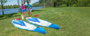 Two blue and white Sea Eagle NeedleNose™ 14 inflatable paddleboards on grass, with people nearby.