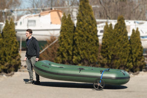 Man pulling a dark green inflatable boat on a black and blue heavy-duty EZ cart with wide wheels.
