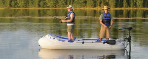 Two men fishing from a white and blue Sea Eagle 9 inflatable boat with an electric motor on a calm lake.