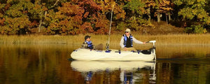 Two people fishing from a white Sea Eagle inflatable boat with an electric motor on a calm lake.