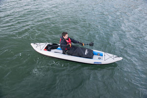 Person kayaking in a white Sea Eagle inflatable kayak with a black waterproof blanket covering their legs.