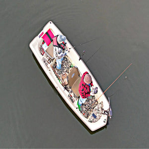 Two anglers in a beige Sun Dolphin American 12 boat with camouflage flooring, fishing on calm water.