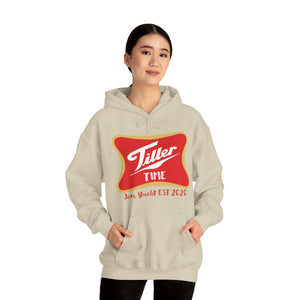 Woman wearing a beige Tiller Time Hoodie with a red and gold graphic, hands in the kangaroo pocket.