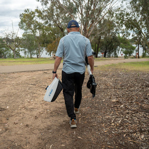Man walking with fishing gear on a path near trees and water