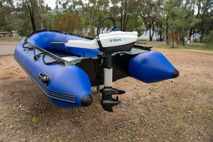 Blue inflatable boat with Bixpy outboard motor on a dirt ground with trees in the background