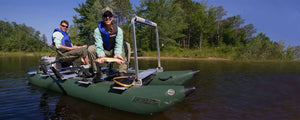 Two men fishing from a dark hunter green Sea Eagle 375fc FoldCat inflatable pontoon boat on a lake.