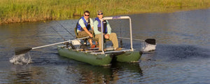 Two men fishing from a dark hunter green Sea Eagle 375fc FoldCat inflatable pontoon boat with oars.