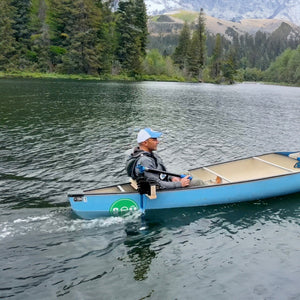 Person paddling a blue canoe on a calm lake with mountains in the background