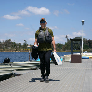 Person walking on a dock with fishing gear, wearing a green shirt and black pants.