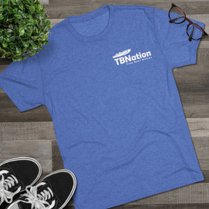 Blue t-shirt with 'TBNation' logo on a wooden surface with sneakers and glasses.