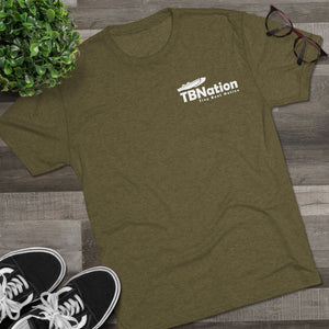 Green t-shirt with a logo on a wooden surface next to sneakers and glasses.