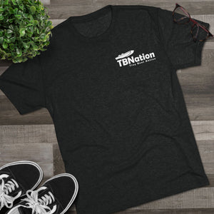 Black t-shirt with 'TBNation' logo on a wooden surface with sneakers and a plant.