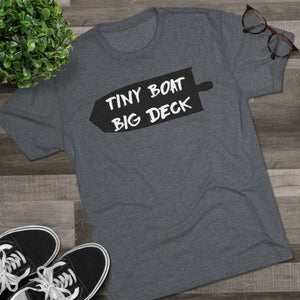 Gray t-shirt with 'Tiny Boat Big Deck' text on a wooden surface with sneakers and a plant.
