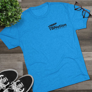 Blue t-shirt with 'TBNation' logo on a wooden surface with shoes and a plant.