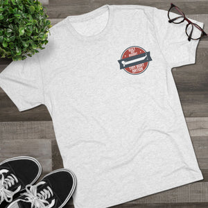 White t-shirt with a red and black logo on a wooden surface with sneakers and a plant.