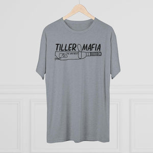 A heather gray short-sleeve t-shirt hanging on a wooden hanger against a white paneled wall. The shirt features a black graphic print on the chest that reads 'TILLER MAFIA' above a drawing of a revolver.