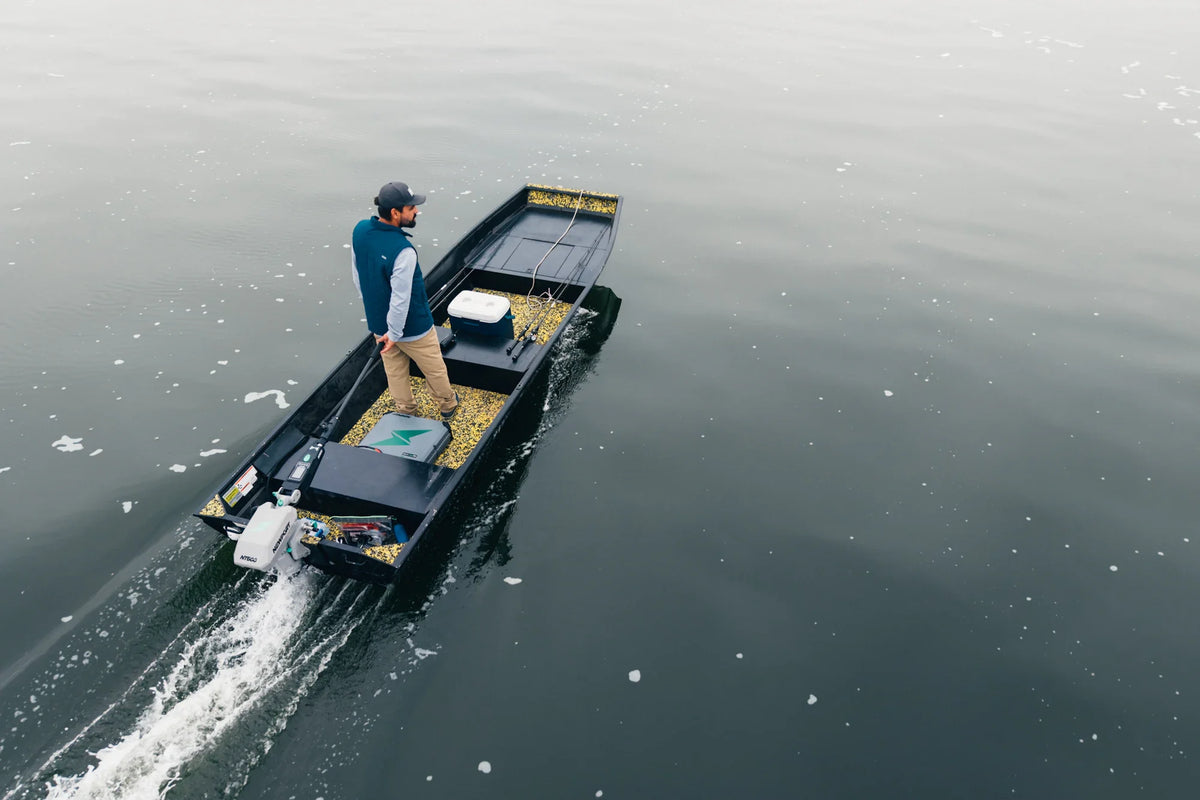 Man in a small, black flat-bottom boat with a white outboard motor, moving across calm water.