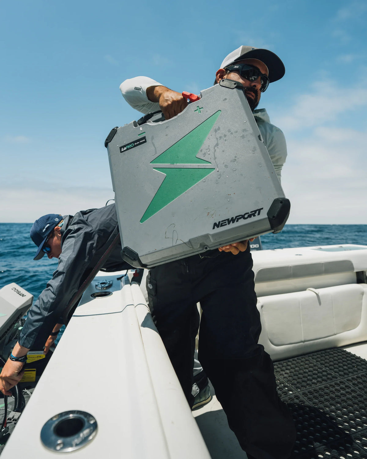 Man carrying a gray Newport LoPRO 48V 70Ah Lithium battery with a green lightning bolt logo on a boat.