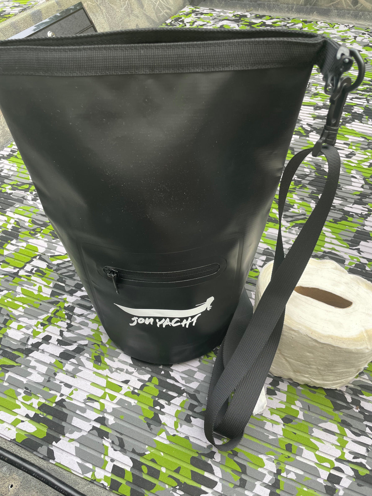 Black 5L Jon Yacht dry bag with front zipper pocket and shoulder strap, next to a roll of toilet paper.