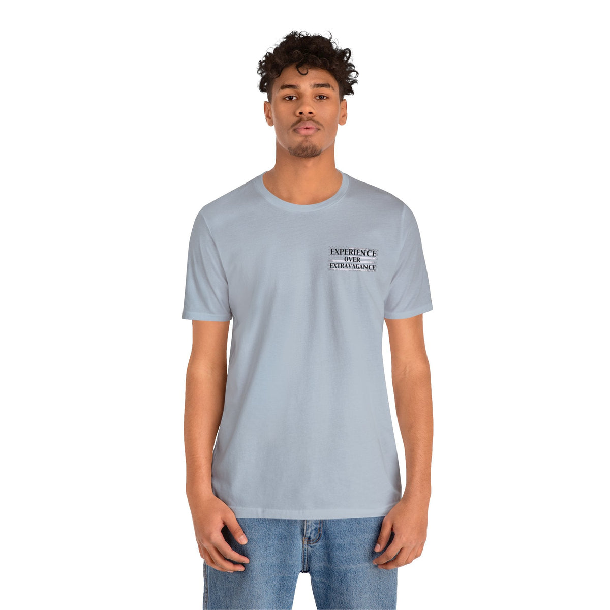 Man wearing a light blue "American Dreamer" unisex jersey tee with "EXPERIENCE OVER EXTRAVAGANCE" text.