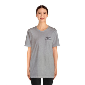Woman in a light gray unisex jersey tee with "EXPERIENCE OVER EXTRAVAGANCE" text.