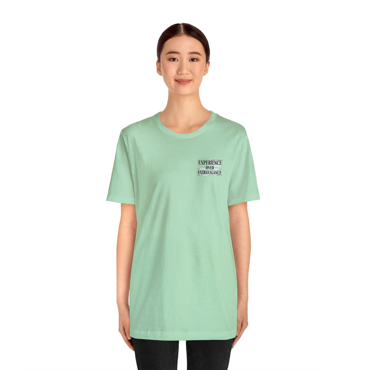 Woman wearing a light green unisex jersey t-shirt with "EXPERIENCE OVER EXTRAVAGANCE" text.
